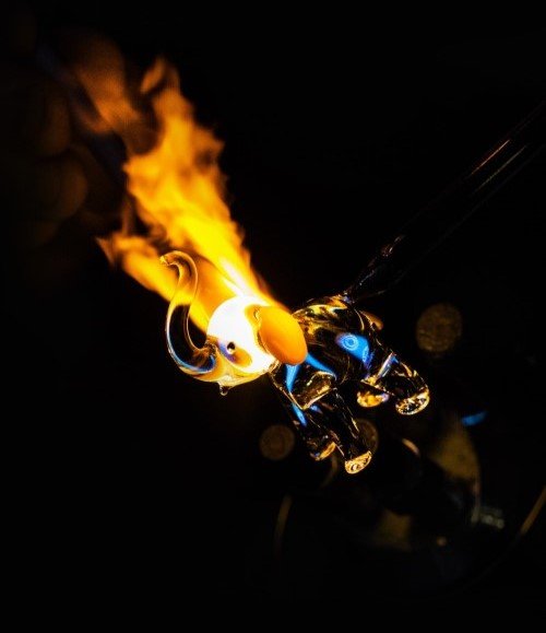 Artisan glassblower shaping a detailed elephant figurine from molten borosilicate glass under intense flame, demonstrating the durability and versatility of our high-quality glass tubes.